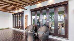 A covered outdoor area with a wooden floor, two wicker chairs, and a glass table. - 888 Residences - Complex of Private Villas with Pools (Ubud)