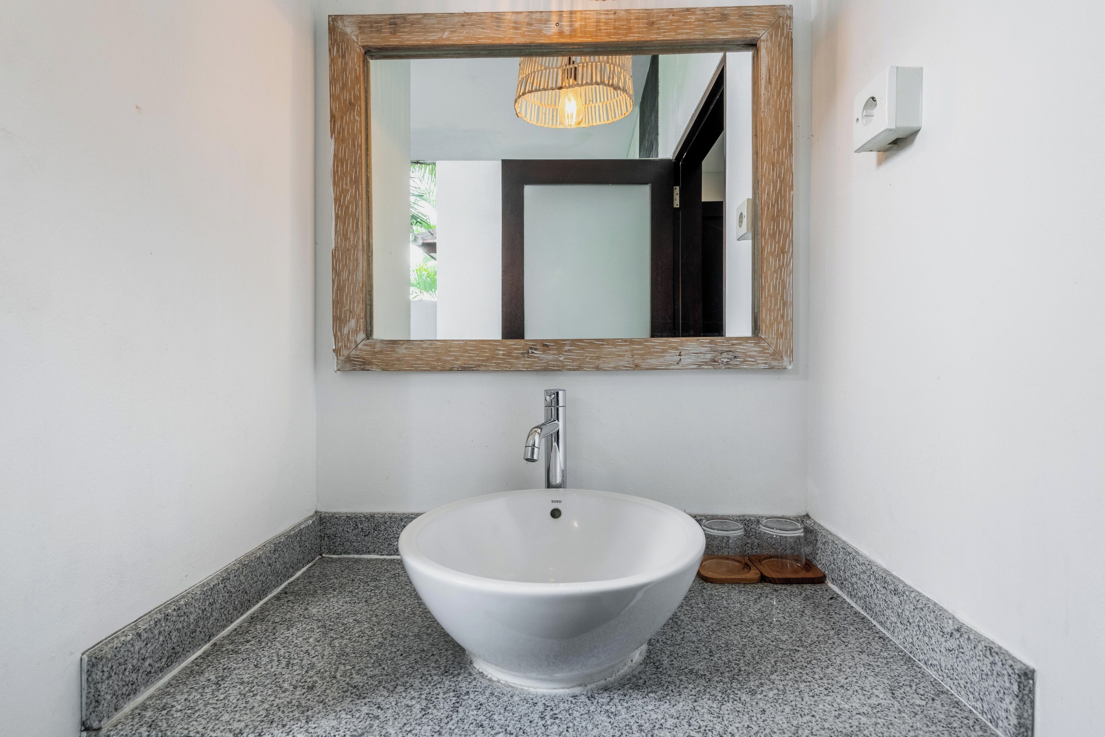 Un baño con un lavamanos de cerámica blanca, un espejo con marco de madera y una encimera de granito.