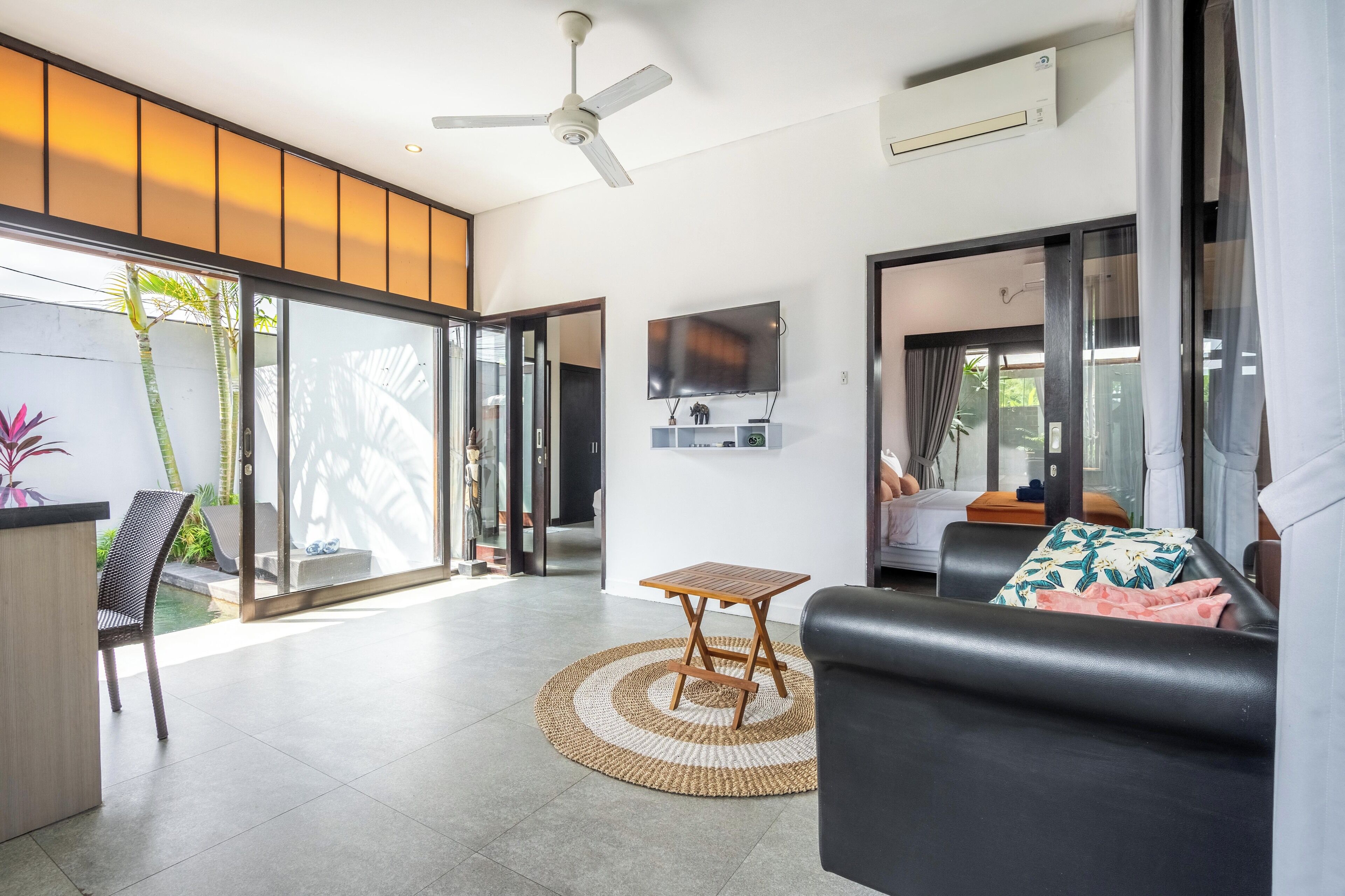 A modern living room with a sofa, a small wooden table, a TV, and a ceiling fan.