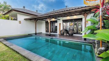 A swimming pool with a covered patio area, a statue, and lush greenery.