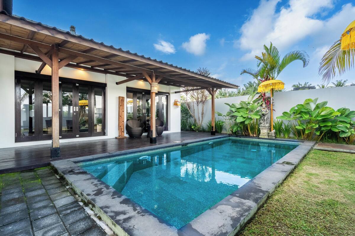 Une piscine rectangulaire dotée d’une terrasse en bois et d’un patio couvert.