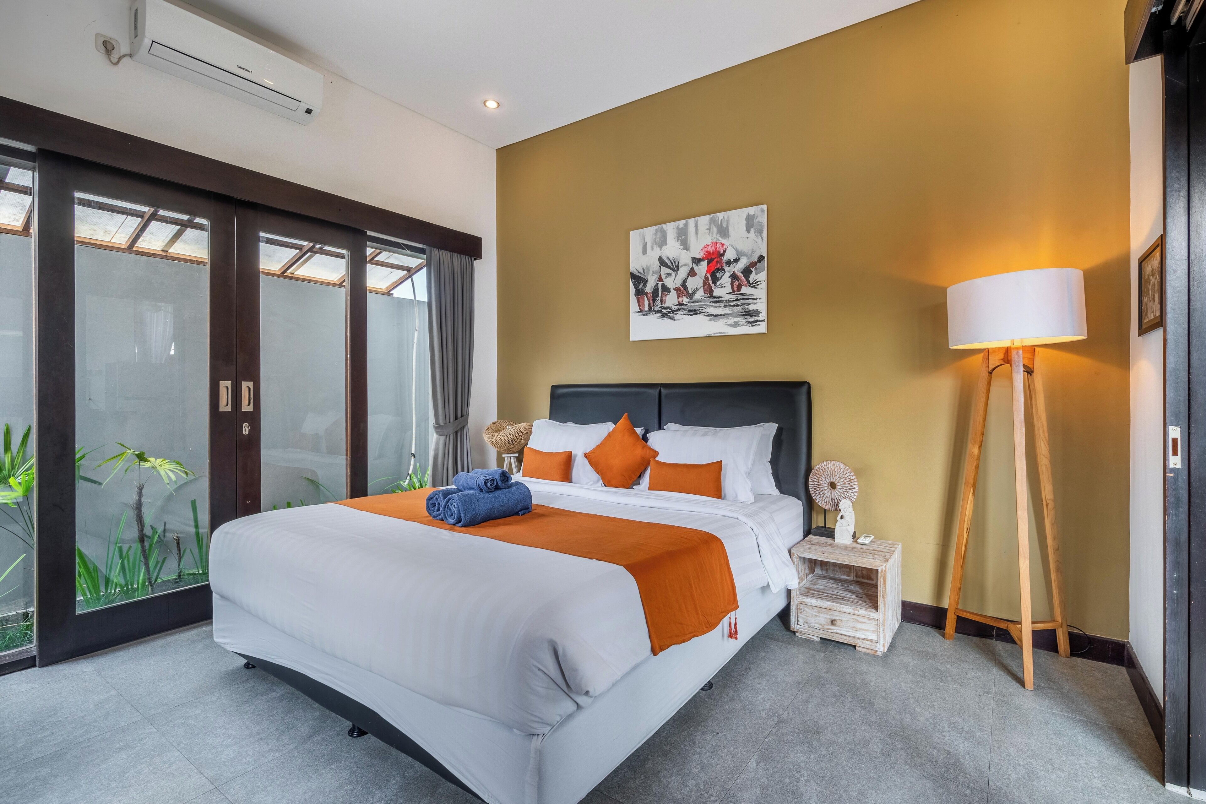 Quarto de hotel moderno com uma cama grande, porta de vidro para uma varanda, um quadro na parede e um abajur.