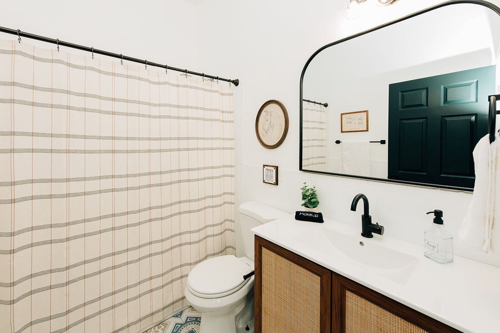 Een badkamer met een gestreept douchegordijn, een toilet, een wastafel met spiegel en een zeepdispenser.