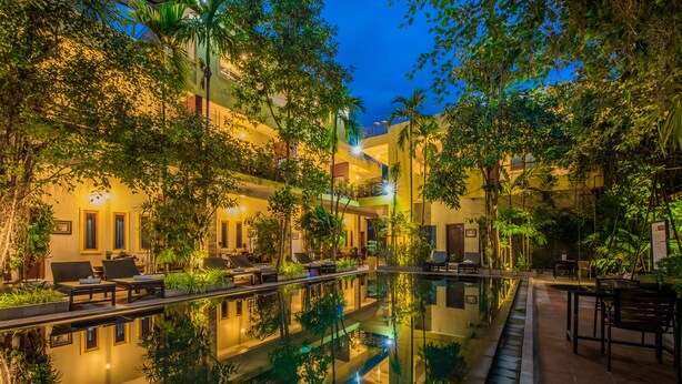Ein Hotelinnenhof mit einem glitzernden Pool, Sitzgelegenheiten im Freien und üppigem Grün.
