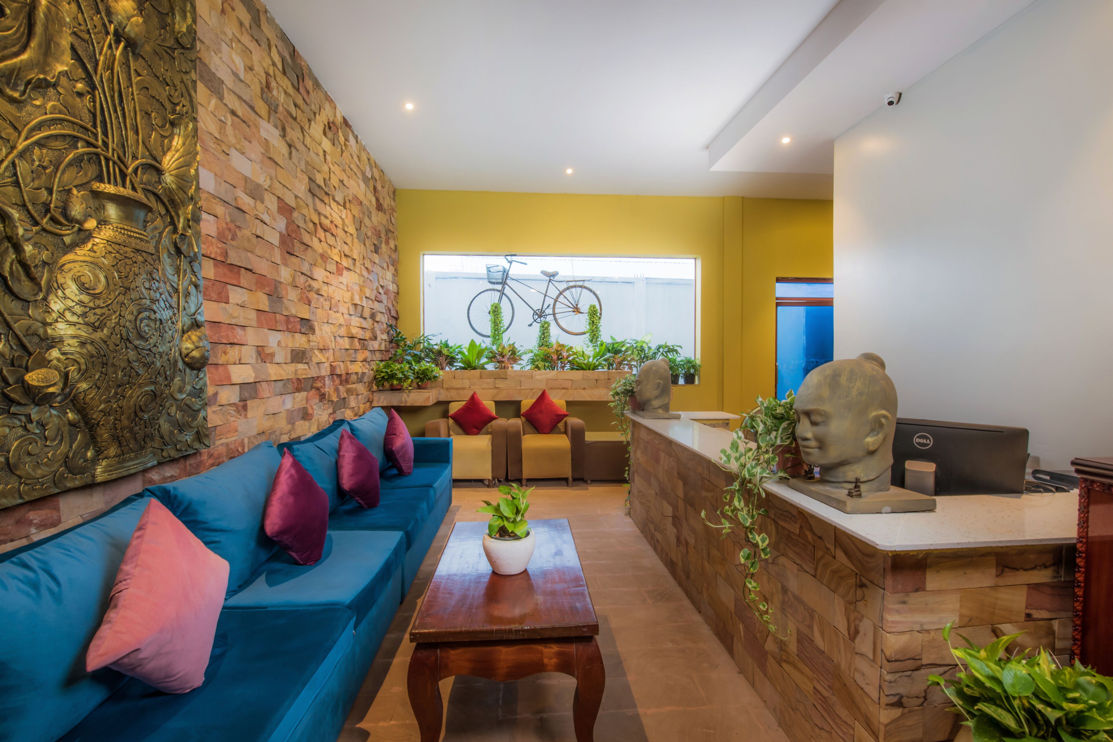 Un hall d’entrée moderne avec un canapé bleu, un comptoir d’accueil et une grande fenêtre donnant sur un vélo.