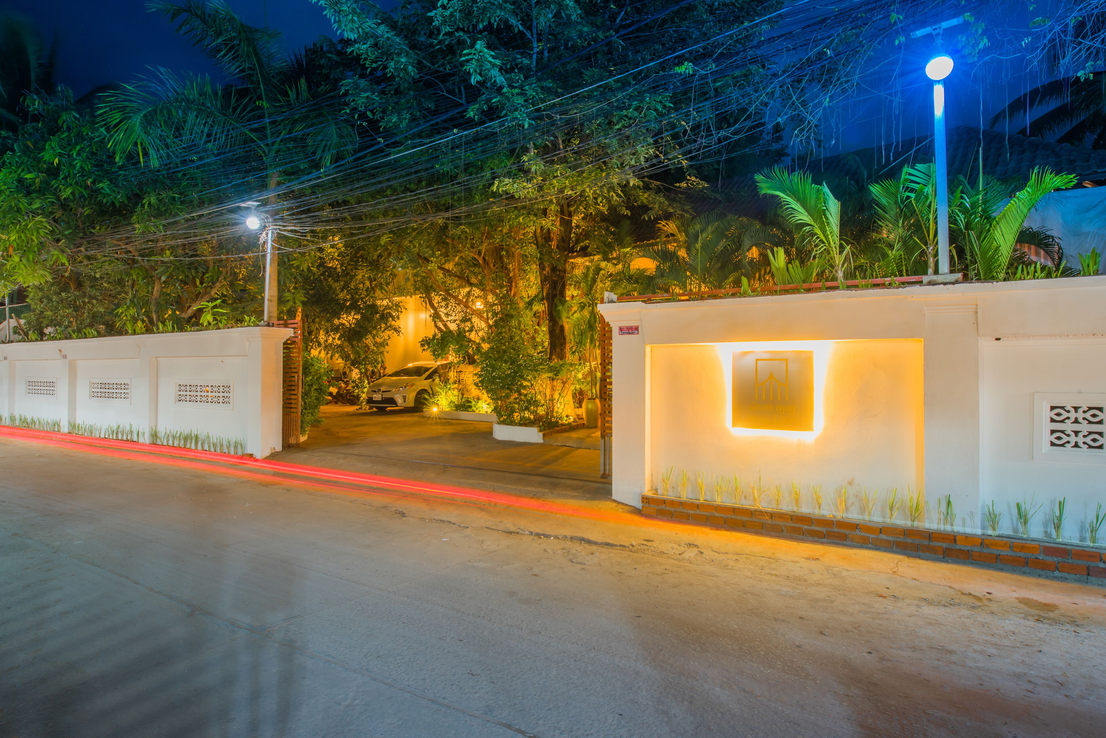A gated entrance with a well-lit pathway, surrounded by lush greenery and palm trees.