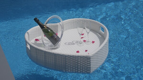 Una cesta de mimbre con una botella y copas junto a una piscina.