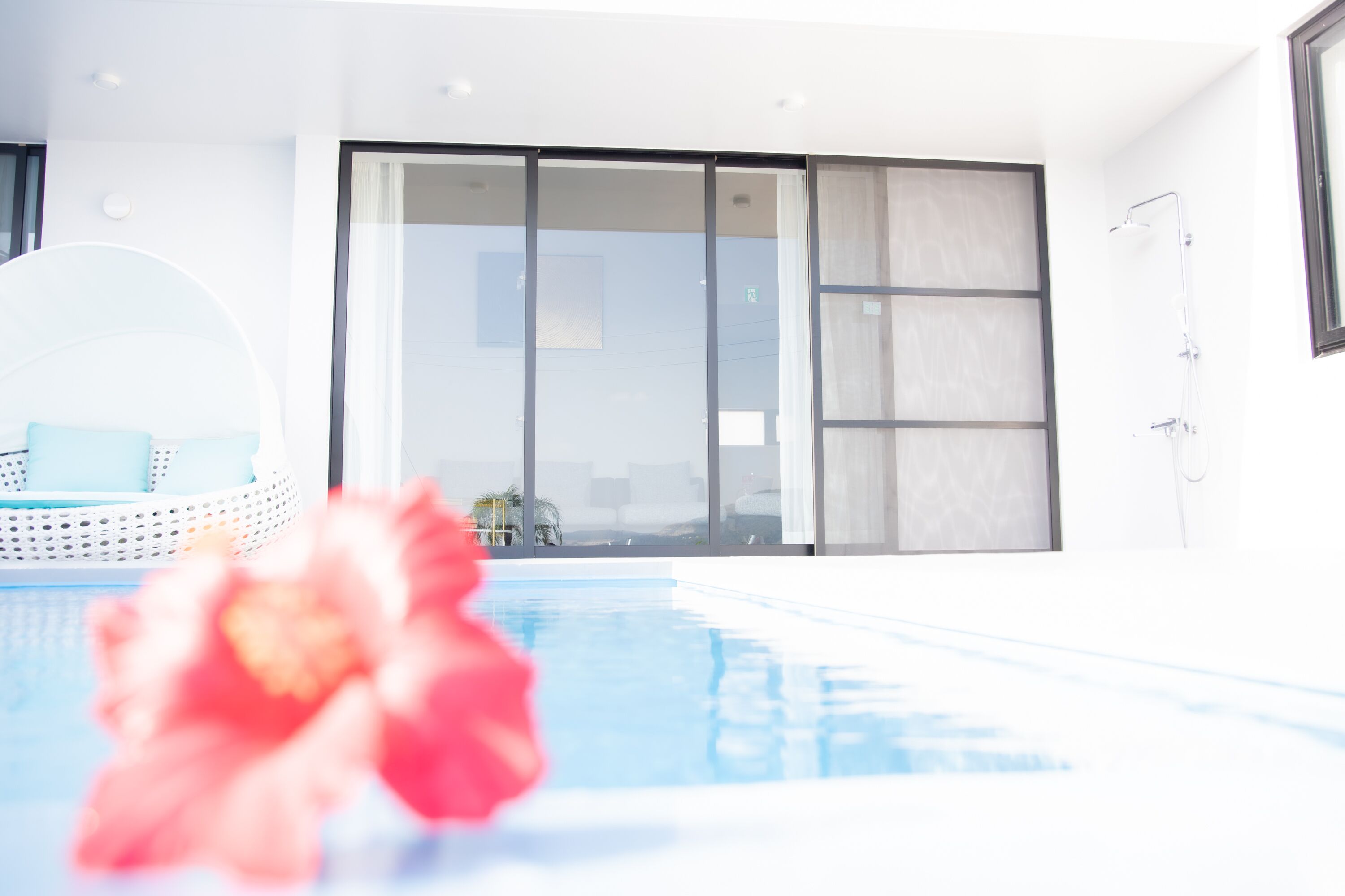 A modern indoor pool area with a clear view of the pool, a seating area with a round chair, and a large sliding glass door leading to an outdoor space.
