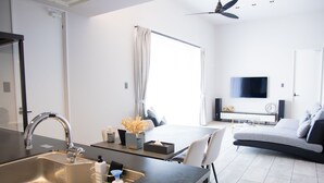 Een moderne keuken met een spoelbak, een eethoek met tafel en stoelen, een bank en een aan de muur bevestigde televisie.