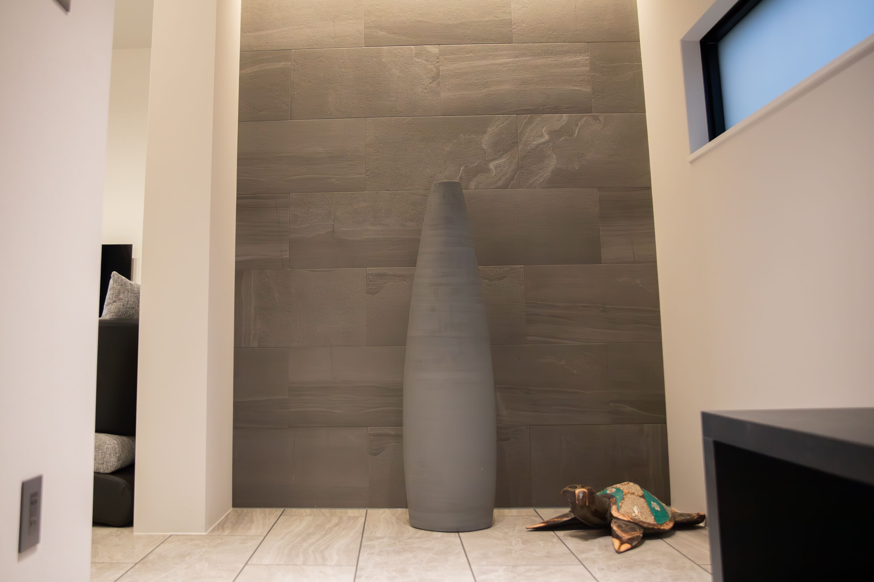 Un pasillo con una gran escultura cilíndrica, una tortuga y un televisor sobre un soporte.