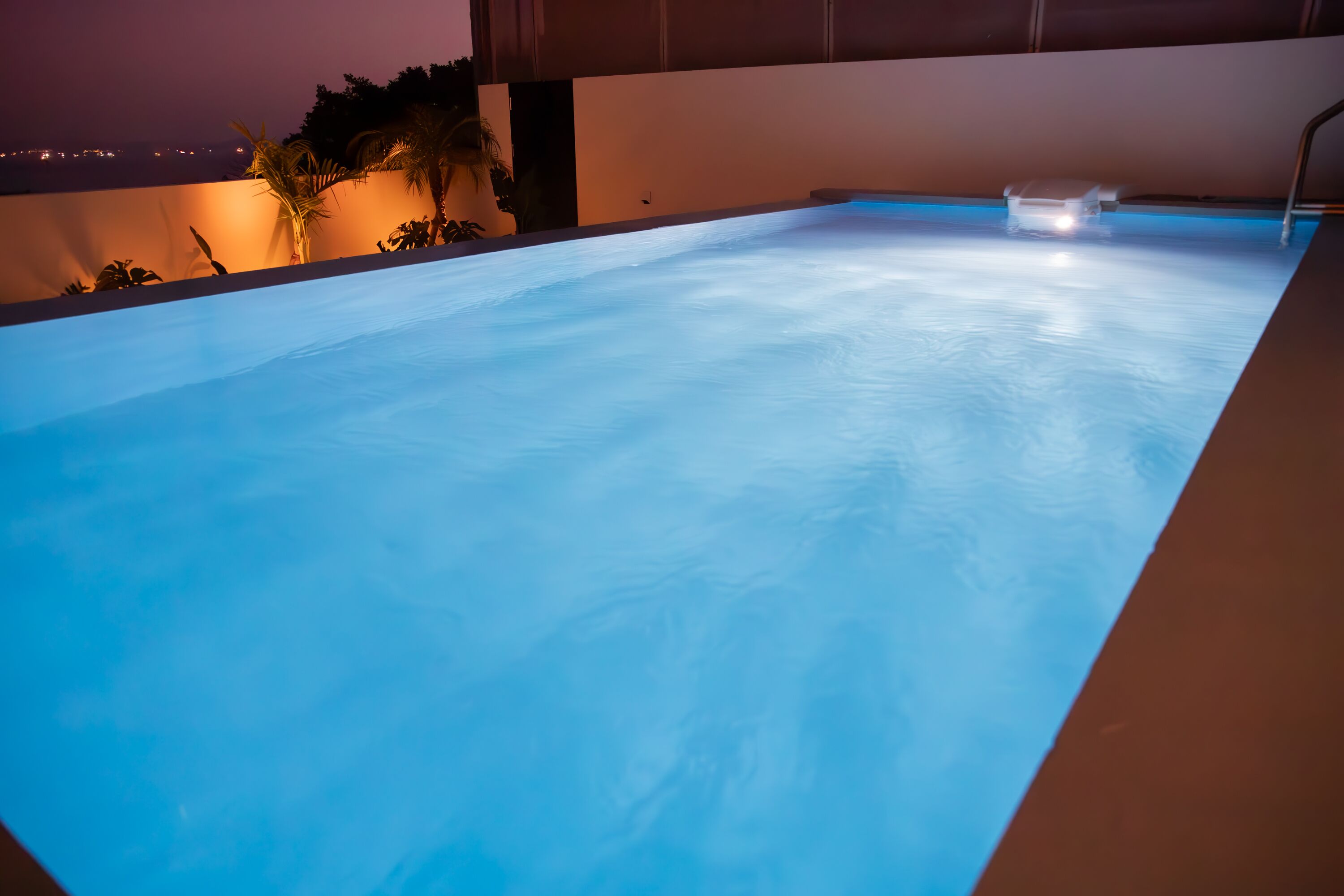 A swimming pool with a clear blue water surface, surrounded by a low wall and some plants.
