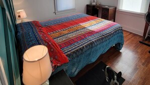 A bedroom with a bed, a ceiling fan, a nightstand, a lamp, and a dog on a rug.