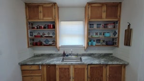 A kitchen with wooden cabinets, a granite countertop, and a window with blinds.