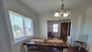 A dining area with a wooden table and bench, a chandelier, and a view through an open door.