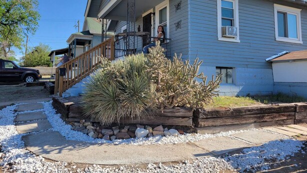 A two-story house with a front porch, a small garden with cacti, and a wooden deck.