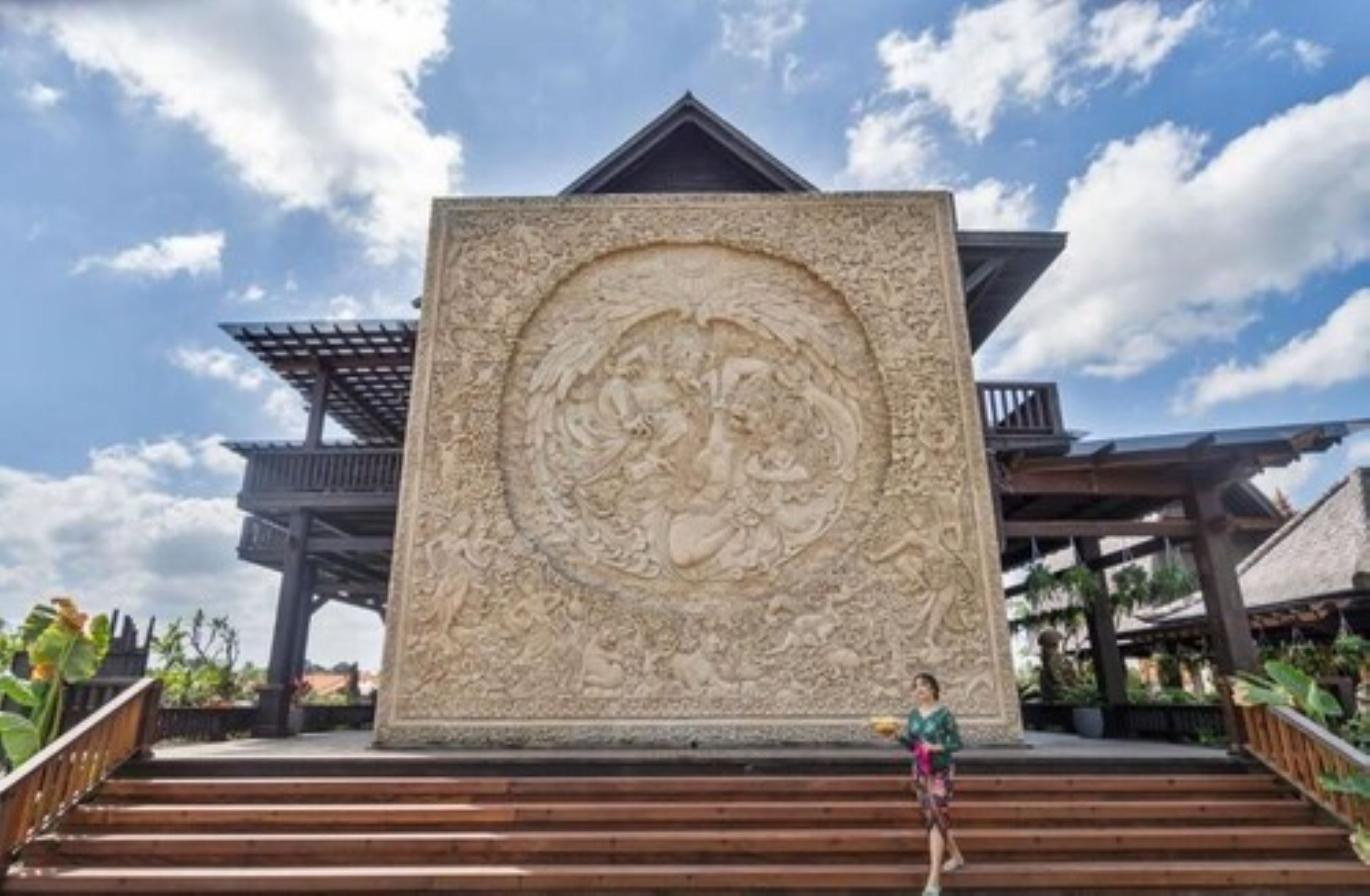 Une imposante structure en pierre, ornée de sculptures complexes, avec des marches en bois menant à son sommet, et un ciel bleu clair en arrière-plan.