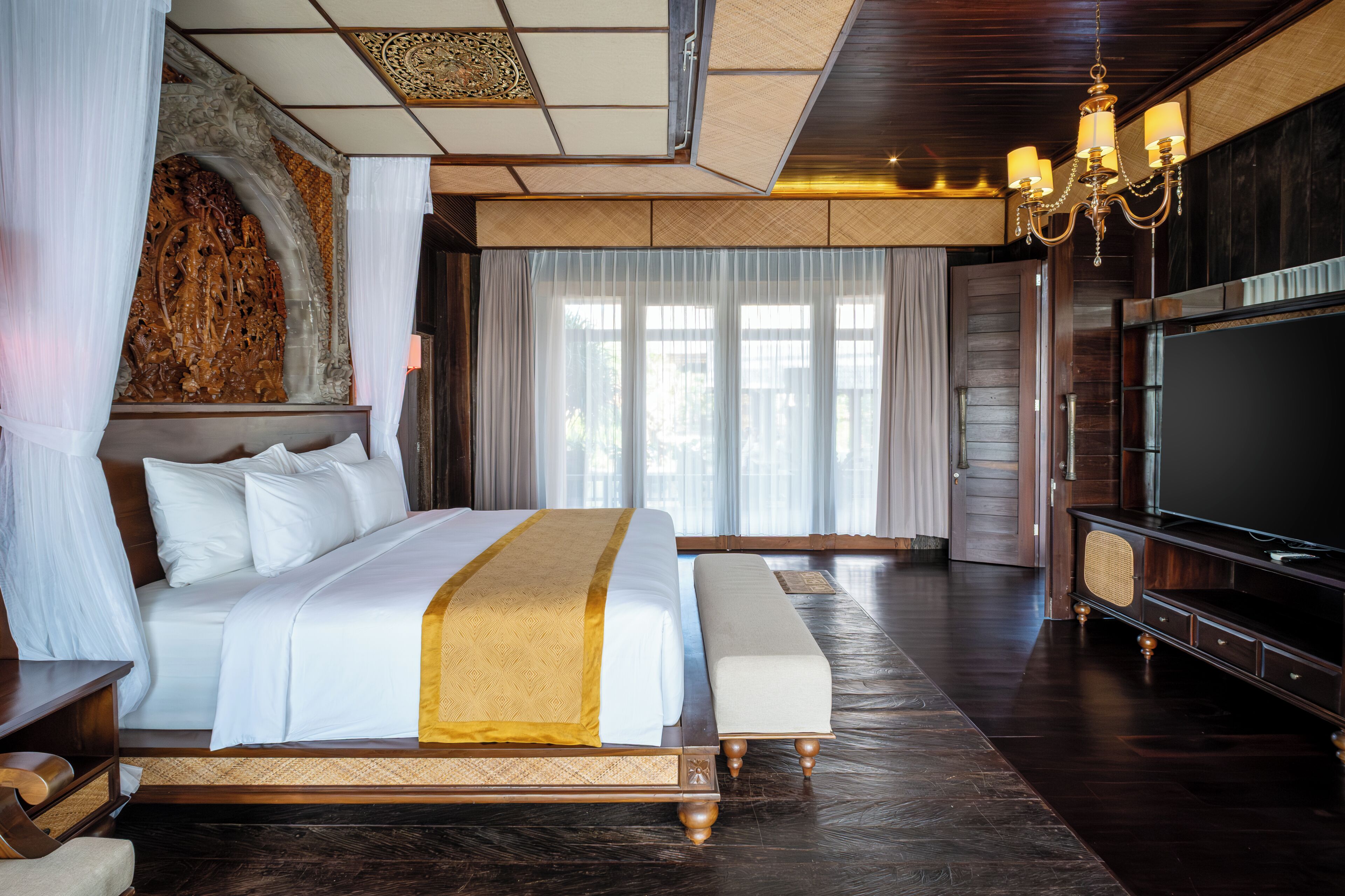 Ein großes Bett mit goldfarbenen Akzenten, ein Fernseher und ein Holzboden in einem Hotelzimmer.