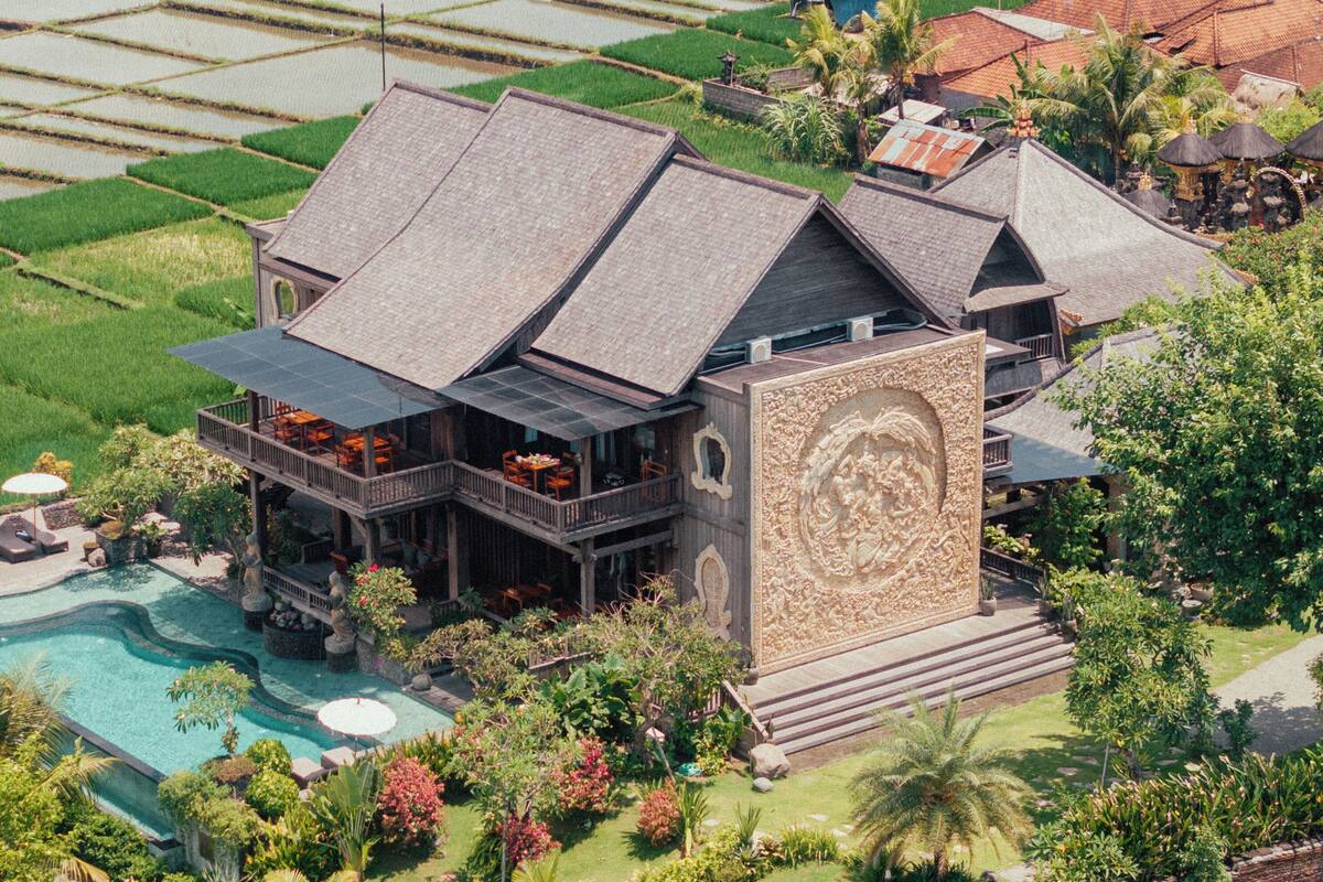 Una casa grande con piscina, rodeada de vegetación exuberante y campos de arroz.