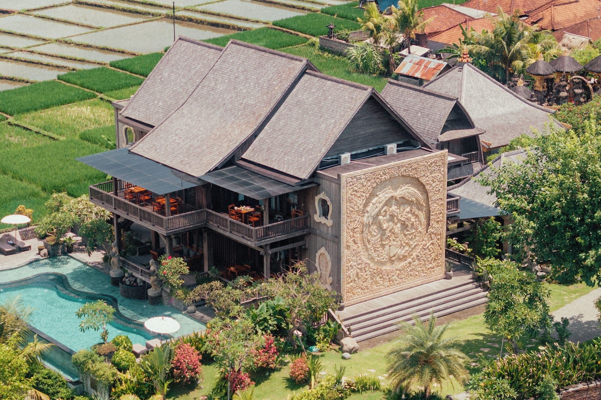 A large house with a pool, surrounded by lush greenery and rice paddies.
