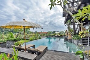 Área de piscina com espreguiçadeiras e um guarda-sol, rodeada por vegetação exuberante e um deck de madeira.
