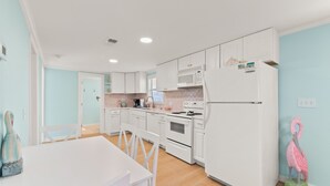 Une cuisine moderne avec des meubles blancs, un four à micro-ondes et un réfrigérateur. On y trouve une table à manger avec des chaises et une statue de flamant rose décorative.