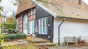 Ein traditionelles Fachwerkhäuschen mit weißer Fassade, einem Ziegeldach und einem kleinen Garten mit Bank und Topfpflanzen.