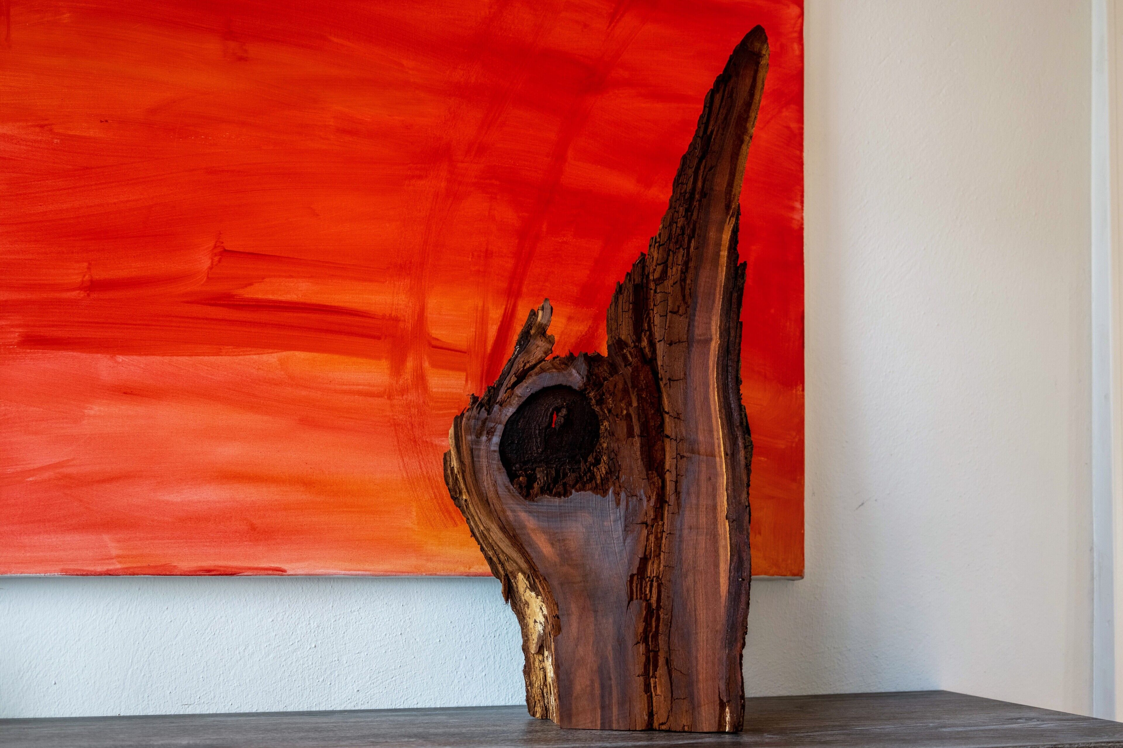 Une sculpture réalisée à partir d’un morceau de bois flotté, placée devant un mur rouge.