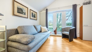 Ein modernes Wohnzimmer mit einer Couch, einem Sessel, Holzboden und Blick durch eine Glastür.