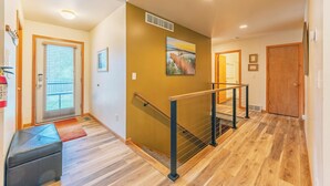 Un interior moderno con suelo de madera, una escalera con barandilla de metal y una puerta que da a otra habitación.
