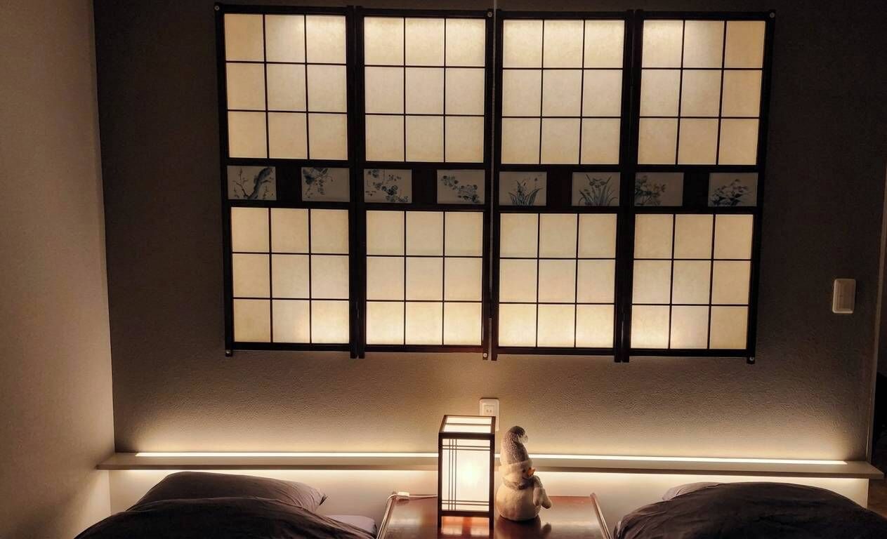 Ett rum med en traditionell skjutdörr med ett rutmönster, ett litet bord med en lampa och en säng med kuddar.