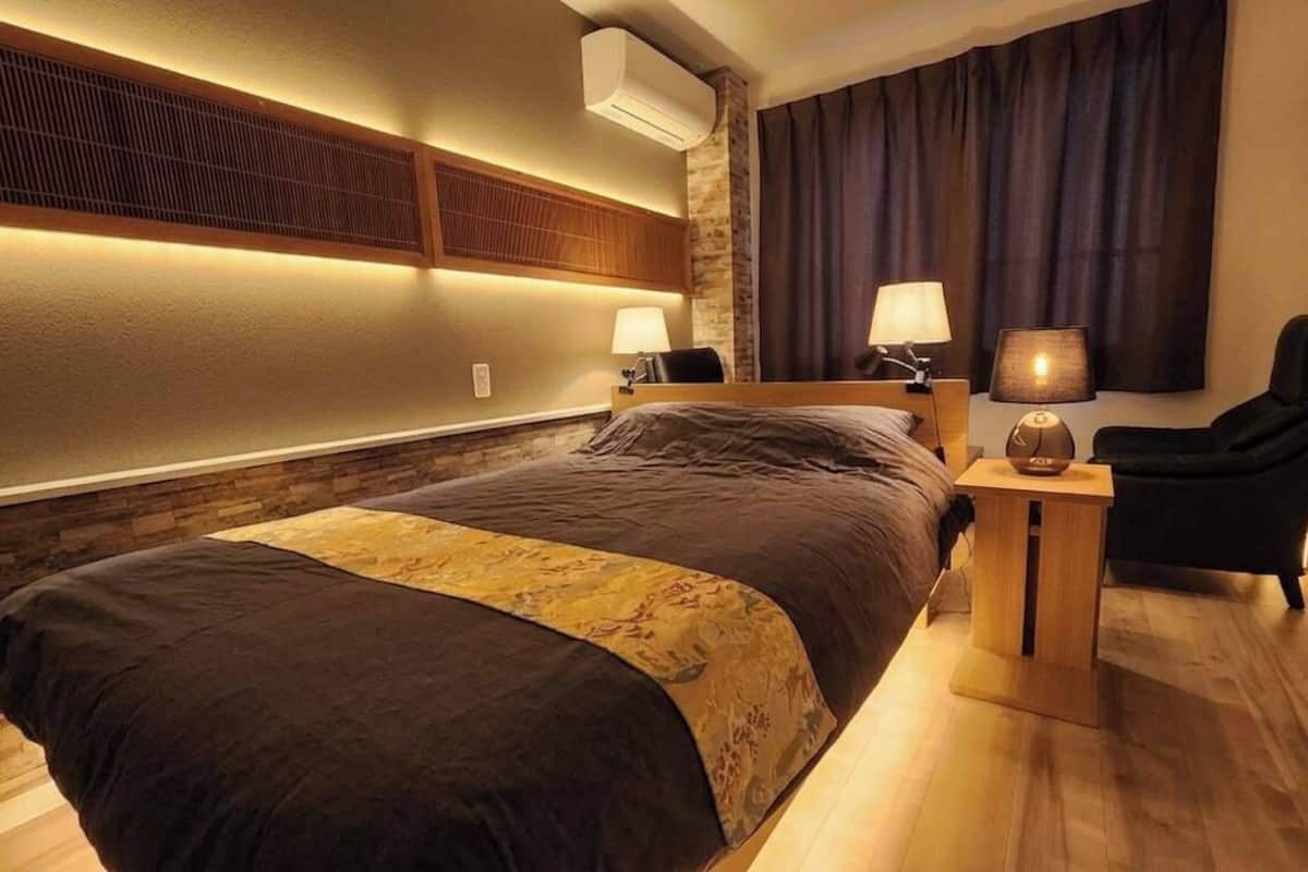 Une chambre d’hôtel avec un lit, des lampes de chevet, une chaise, une table de chevet et une fenêtre avec des rideaux.