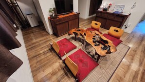 Een eethoek met een houten tafel, rode kussens en een geweven mat.