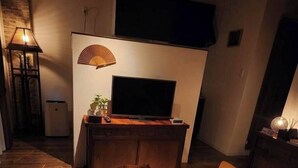 Een gezellige woonkamer met een flatscreen televisie, een houten bijzettafeltje en rode kussens.