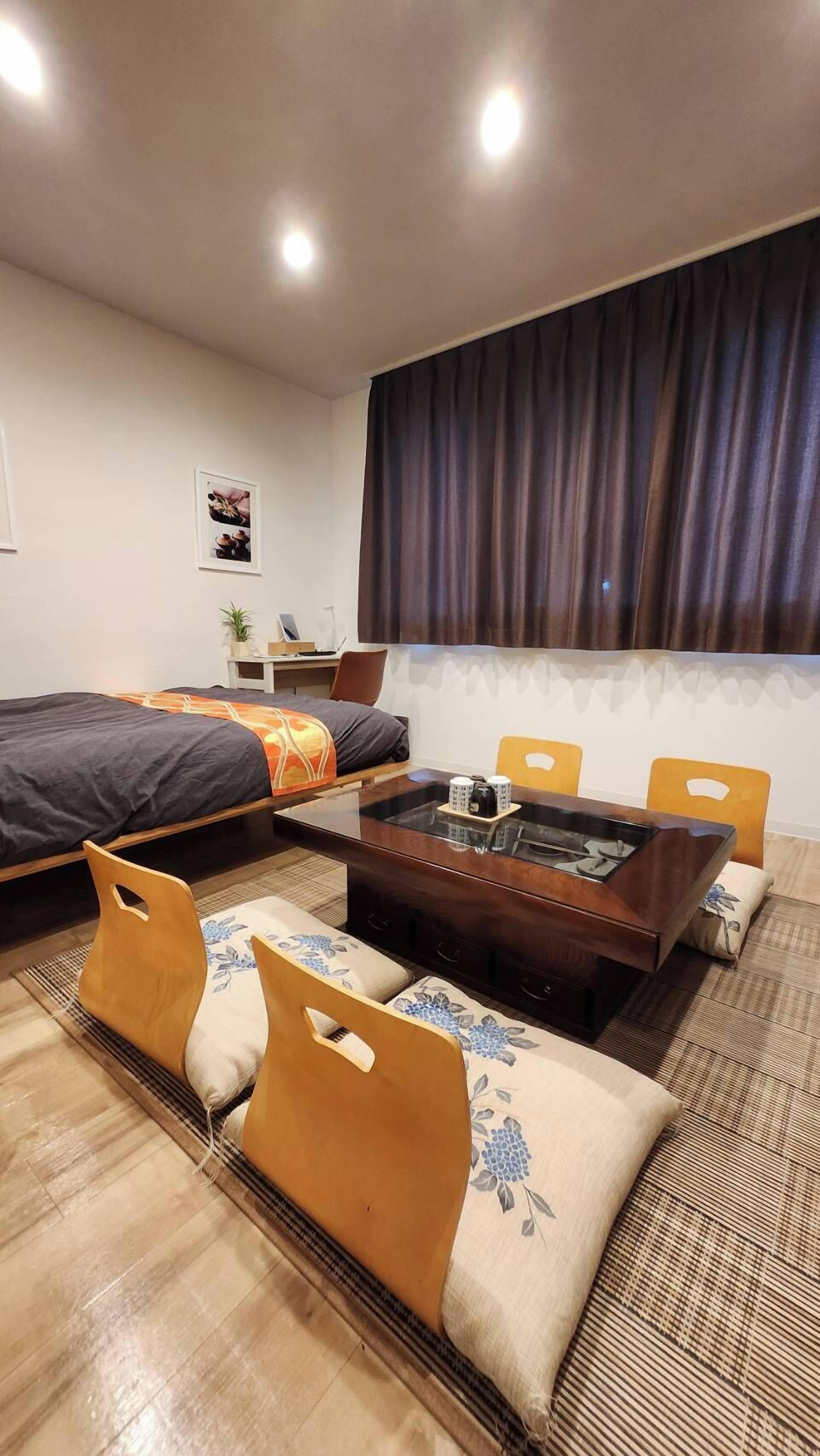 Habitación de hotel moderna con cama, mesa de comedor, sillas, sofá, pequeño escritorio y ventana con cortinas.