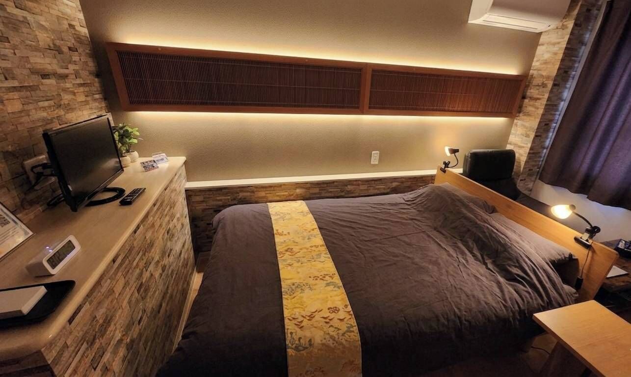 Een hotelkamer met een bed, een bureau met een computer, een televisie en een wandplank.