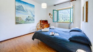 A bedroom with a bed, a chair, a painting, a window, and a radiator.