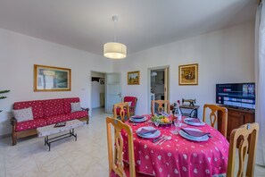 A dining area with a table set for four, a sofa, and a television.