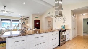 Una cocina moderna con armarios blancos, encimera de granito, electrodomésticos de acero inoxidable y un ventilador de techo.