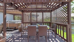 Un patio cubierto con techo de enrejado de madera, mobiliario exterior y vista al follaje circundante.