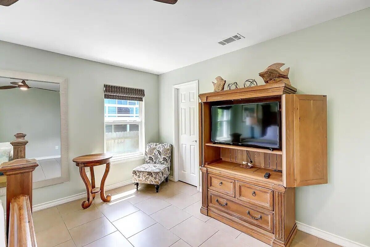 Una sala de estar con un mueble de entretenimiento de madera, un sillón estampado y una mesita redonda.