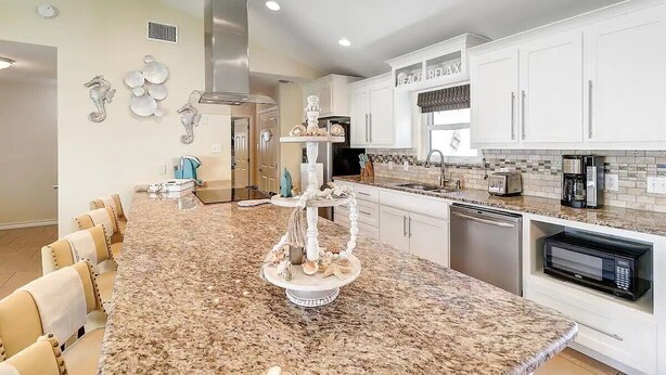 Una cocina moderna con armarios blancos, encimeras de granito y una isla central decorada.