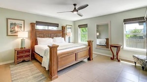 Un dormitorio con una cama grande, un ventilador de techo, una mesita de noche, un espejo y una ventana con vistas al exterior.