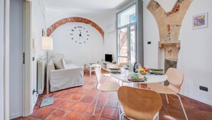 Una sala de estar con un sofá blanco, una mesa de comedor con sillas, una chimenea de ladrillo y un ventanal grande.