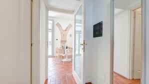 Un pasillo con suelo de baldosas, una puerta blanca y una puerta de cristal que da a un comedor con sillas y una mesa.