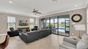 Un salón amplio con un sofá modular, un sillón gris, una zona de comedor con vista a la piscina y un ventilador de techo.