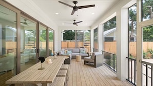 A covered patio with a wooden deck, a sofa, a table, and ceiling fans.