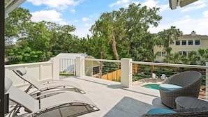 A covered outdoor area with lounge chairs, a small pool, and a view of surrounding trees and buildings.