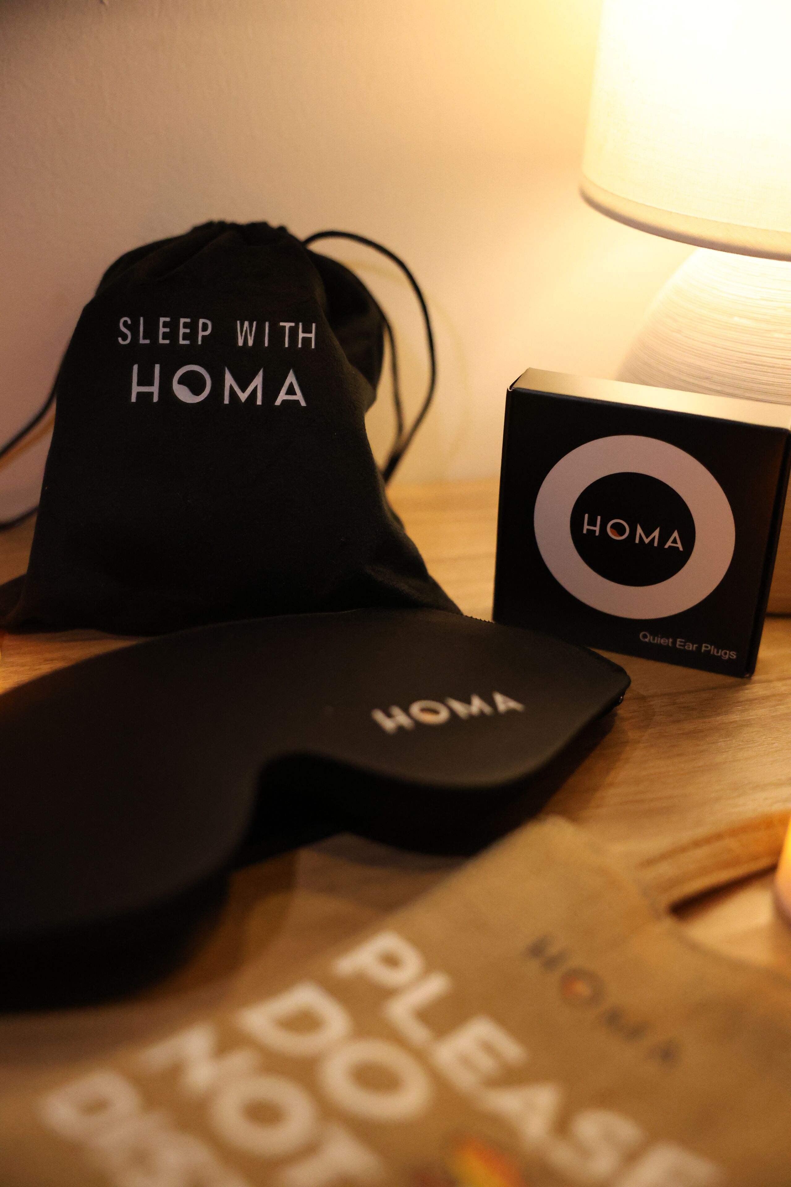 Een zwarte tas met de tekst 'Sleep with HOMA', een zwarte doos met de aanduiding 'HOMA Oordoppen voor een rustige nacht', en een zwart object met 'HOMA' tekst.