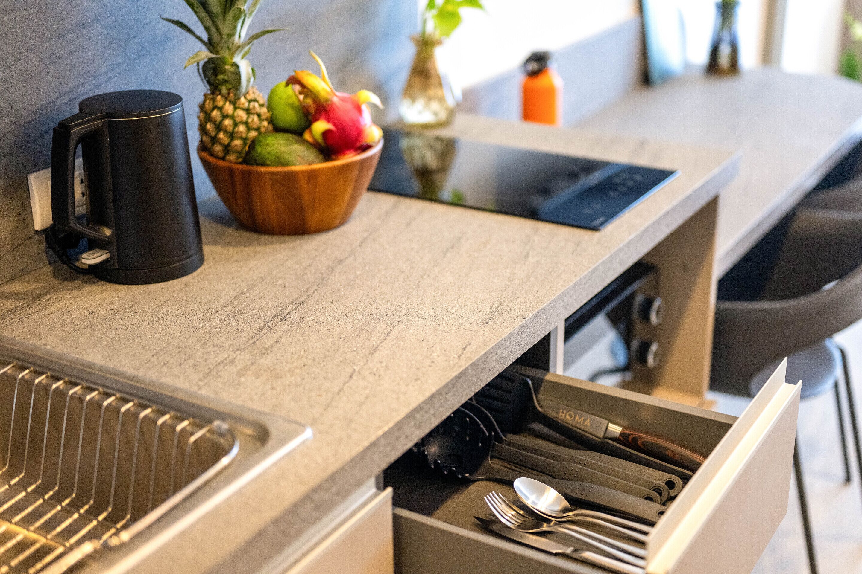A kitchen counter with a coffee maker, a fruit bowl, and a drawer with utensils.