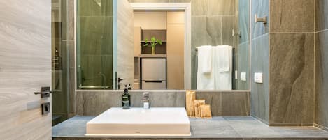 A modern bathroom with a large mirror, a white sink, and a glass shower enclosure.